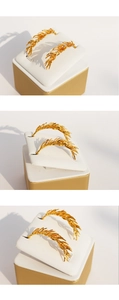 Detailed macro view of golden wheat ear earrings with textured metallic finish on stand