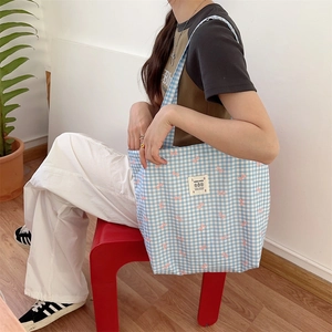 Detail of blue plaid canvas tote bag with pink bow print and shoulder strap on model