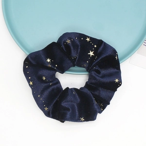 Macro detail of navy velvet hair scrunchie with gold star pattern on a blue tray
