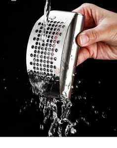 Water rinsing a professional curved stainless steel garlic press with dense round holes