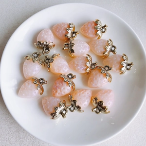 Macro shot of 13 pink resin strawberry charms with gold leaves on a white ceramic tray