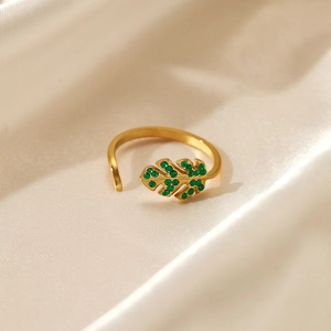 Adjustable golden leaf ring with green crystals on a premium silk fabric background