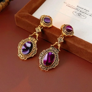 Vintage gold-toned hollow engraved earrings with oval purple stones on a leather box