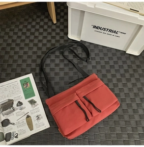 Detail of brick red nylon crossbody bag with dual utility pockets and black drawstrings