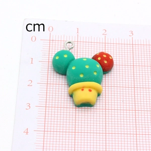 Top view of a green cactus charm with ladybug spots on a metric scale measurement mat
