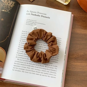 Brown fabric scrunchie with From Sheep label on an open book in soft natural light