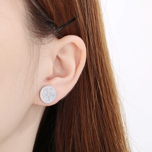 Detail of silver floral stud earrings with centered crystal on a female model