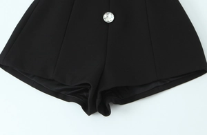 Detail of high waist black romper featuring a large faceted crystal button on the waistband