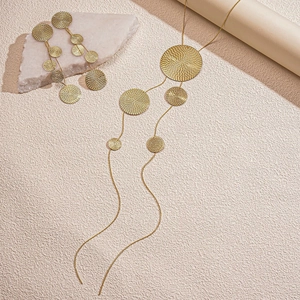 Detail of long gold tassel necklace and earrings with textured geometric circular disks