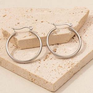 Detailed close-up of silver stainless steel hoop earrings on natural stone surface