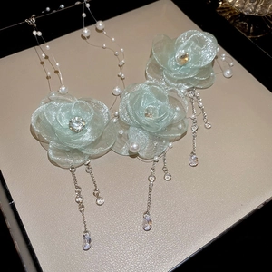 Green fabric flower necklace with pearls and rhinestone tassels on a beige display tray
