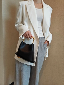 Detail of black leather bucket bag featuring a unique gold metal handle and soft texture