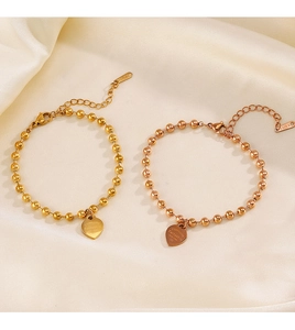 Detail of gold and rose gold stainless steel bead bracelets with heart pendants on silk