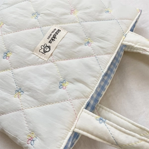 Detail of cream quilted tote bag showing colorful flower embroidery and blue gingham lining