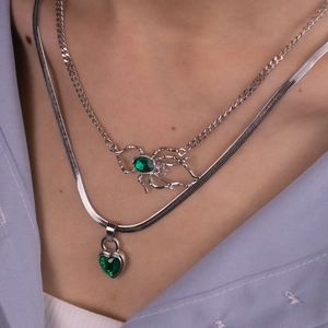 Close-up of layered silver necklaces with green emerald heart and spider pendants