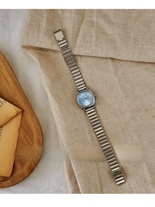 Close-up of a vintage silver ladies watch with a sunburst light blue dial and metal link strap