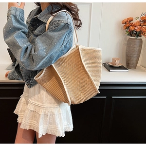 Spacious woven straw tote bag with white trim shown on shoulder for daily summer style