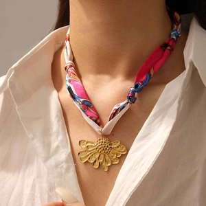 Détail d'un pendentif fleur dorée associé à un foulard en soie imprimé rose et bleu