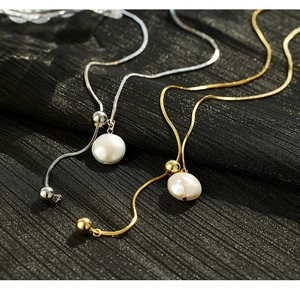 Detailed macro of gold and silver snake chains with baroque pearls on black pleated fabric
