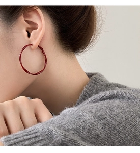 Close-up of deep red twisted hoop earrings with glossy wavy texture on female model