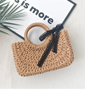 Close-up of handwoven straw handbag featuring a black lace bow on a textured background
