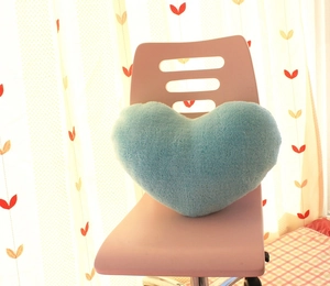 Close-up of a light blue heart-shaped plush pillow on a pink chair with soft textures
