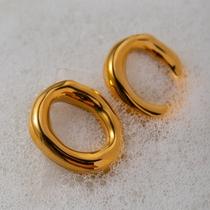 Close-up of chunky gold-plated oval earrings submerged in white soap bubbles for texture