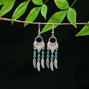 Detailed view of silver ethnic earrings with blue beads and feather tassels on a branch