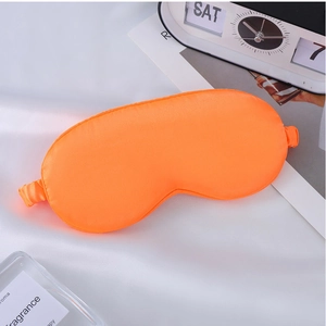 Detailed view of an orange satin sleep mask on a cozy white fabric background