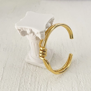 Detail of gold-plated twisted brass cuff bracelet on a white Roman column display
