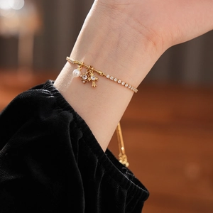 Detailed view of a gold-plated bracelet with zircon cross, star charms and a pearl