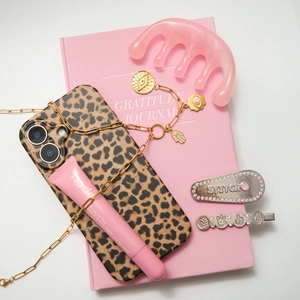 Flat lay van gouden parelketting met luipaardhoesje en modeaccessoires