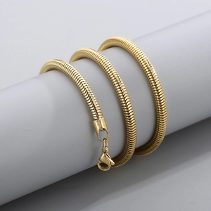 Vista de cerca de un collar de cadena de serpiente de acero titanio dorado sobre cilindro