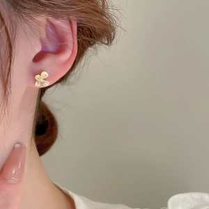 Gros plan d'une boucle d'oreille fleur à quatre feuilles dorée sur l'oreille