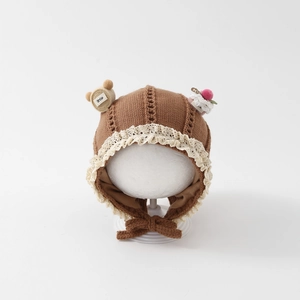 Close-up of brown knit baby bonnet with white lace trim and cute bear embellishments