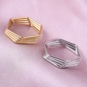 Polished gold and silver hexagonal multi-layer stackable rings on pink silk background