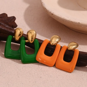 Detailed close-up of geometric green and orange enamel earrings with gold plating on wood
