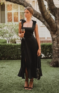 Detail of elegant black midi dress featuring shoulder bows and ruffled slit hemline
