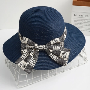 Navy blue straw sun hat with decorative black and white checkered bow and wide brim