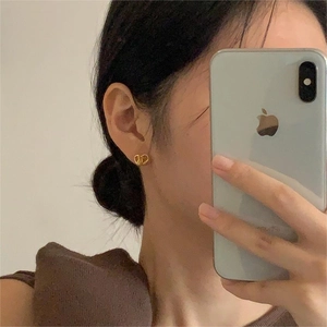 Close-up of golden CD logo stud earrings worn by a model in a minimalist style