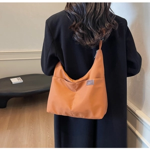 Close-up of an orange-brown nylon tote bag with fashion label and side pocket detail