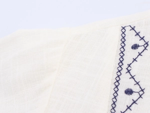 Close-up of ethnic blue embroidery on breathable beige linen fabric blouse texture