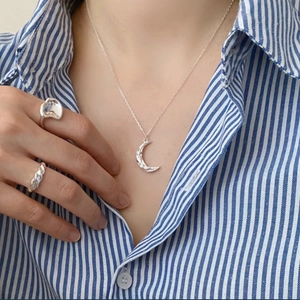 Detail shot of hammered crescent moon pendant necklace and irregular silver rings on a model