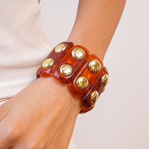 Detail of amber acrylic bracelet with gold studs worn over a white ribbed sleeve