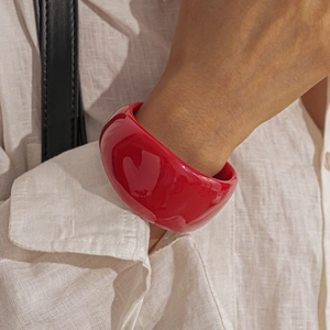 Close-up of a wide glossy red acrylic bangle worn with a linen shirt for a chic vintage look