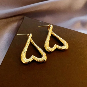 Close-up of golden heart earrings with a hammered metal texture on silk background