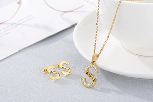 Detail of gold letter S necklace and studs with SMILE engraving and small crystals