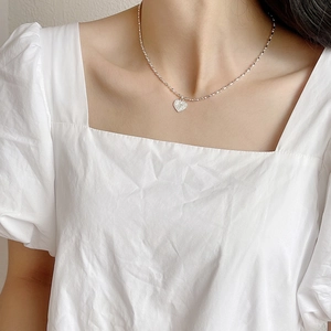 Close-up of sparkling heart pendant on a thin silver chain worn with a white dress