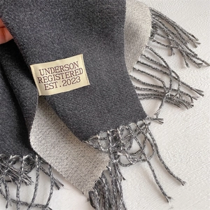 Detailed texture of dual-sided cashmere-like scarf with fringe edges and brand label