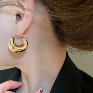 Close-up of chunky gold C-shaped hoop earrings with a high-shine metallic finish